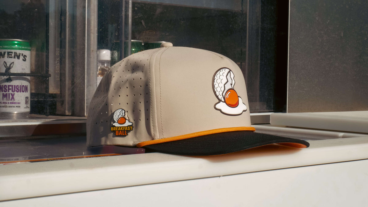 Logie Joe's Golf Breakfast Ball tan snapback hat with built-in magnetic ball marker holder and included marker. Adjustable fit.
