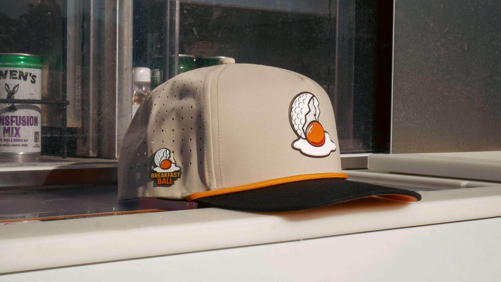 Logie Joe's Golf Breakfast Ball tan snapback hat with built-in magnetic ball marker holder and included marker. Adjustable fit.